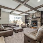 Cozy living room with stone fireplace, exposed wood ceiling beams, built-in cabinetry, leather recliners, and large window with natural light.