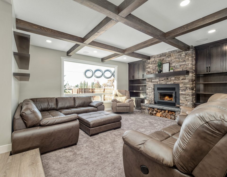 Cozy living room with stone fireplace, exposed wood ceiling beams, built-in cabinetry, leather recliners, and large window with natural light.